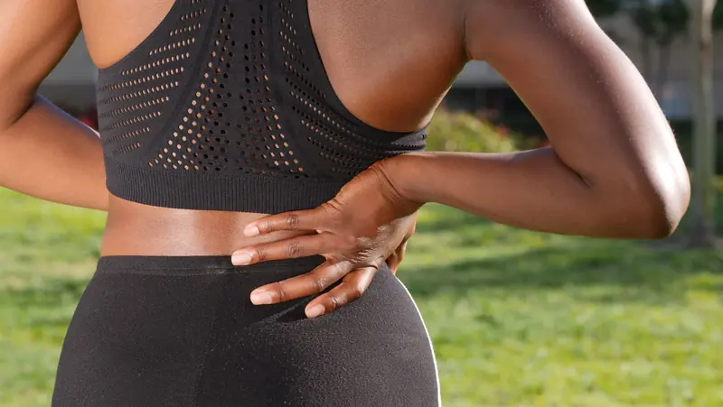Une femme en tenue de sport se tient le bas du dos