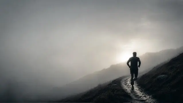 Un coureur monte un chemin dans la brume, face au soleil
