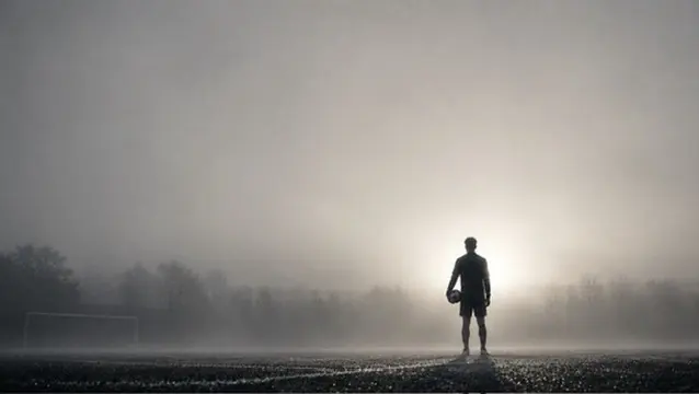 Un footballeur, ballon sous le bras, sur un terrain dans la brume
