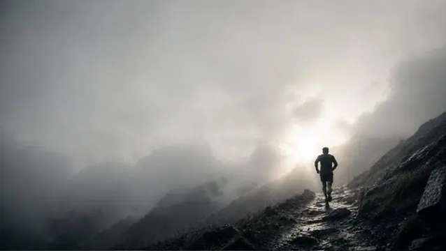 Un coureur sur un sentier de montagne escarpé, dans les nuages